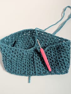 Flat lay picture of a crochet hook and blue yarn cowl