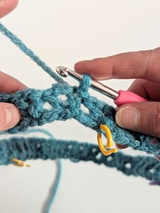 Two hands holding a pink handle crochet hook and piece of crochet in a circle