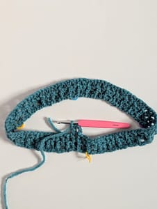 Pink crochet hook against piece of crochet in a circle on a white background