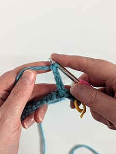 Two hands holding a crochet hook and blue yarn, with crochet chain stitches