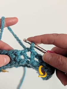 Two hands holding a close up piece of crochet in blue yarn