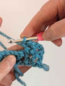 Two hands holding a crochet hook and blue yarn