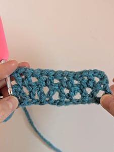 Two hands holding a piece of crochet in blue yarn in V stitch pattern
