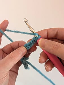 Two hands holding some chain stitches in blue yarn