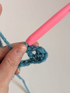 A hand holding a crochet hook and a piece of crochet in blue yarn