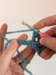 Two hands, a pink handle crochet hook, and blue yarn