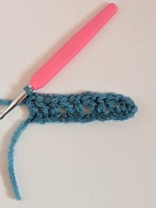Pink handled crochet hook, and a row of crochet in blue yarn