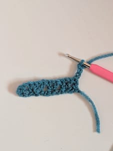 crochet hook with pink handle and a piece of crochet in blue yarn