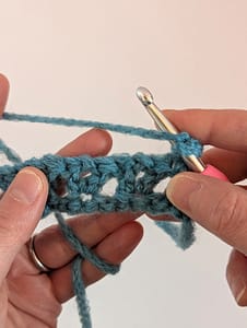 Two hands holding a piece of crochet, ready to work the next crochet V stitch