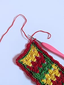 End of red yarn border being added to a granny stripe pattern bookmark