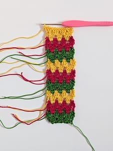 A strip of crochet in granny stripe pattern in green, red and yellow pattern, with ends not weaved in