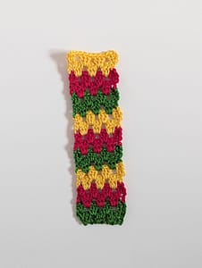 A long strip of crochet in granny stripe pattern in green, red and yellow yarn