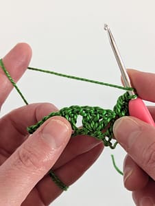 two hands holding a piece of crochet in green yarn