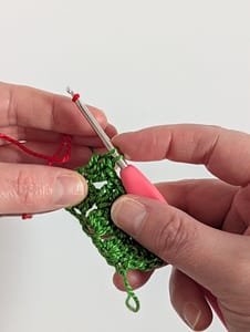 red yarn about to be pulled through the last 2 loops of green yarn in crochet