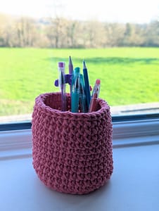 Pink crocheted pencil holder which is holding pens and pencils