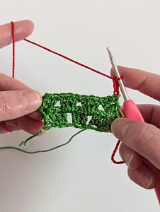 Two rows of double crochet stitches worked as granny stripe stitches, in green yarn, with 3 chain stitches in red