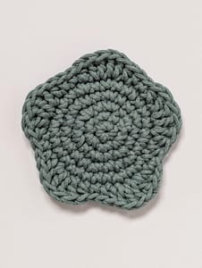 A sage green crochet coaster in the shape of a star