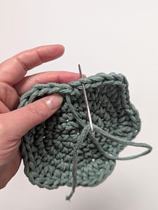The yarn tail being threaded through the previous loop for the invisible join
