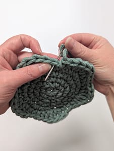 The yarn tail being threaded through the next stitch with a yarn needle for the first step of the invisible join