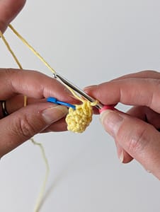 Two hands holding a crochet hook and some single crochet stitches in yellow yarn