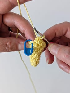 Two hand holding a crochet hook and some single crochet stitches creating the shape of cone in yellow yarn
