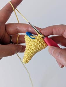 Two hand holding a crochet hook and some single crochet stitches creating the shape of a cone in yellow yarn