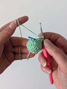Two hands holding a crocheted small cone shape in mint green yarn