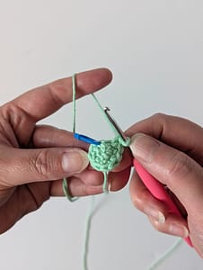 Two hands holding a crochet hook and some single crochet stitches in the round in mint green yarn