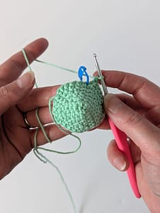 Two hands holding a pink handled crochet hook and crochet stitches worked in the round to create a curved piece of crochet fabric