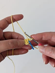 Two hands holding a crochet hook and some crochet stitches in yellow yarn