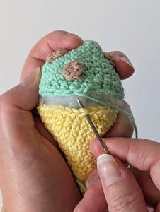 The top and bottom pieces of a crocheted ice cream being sewn together