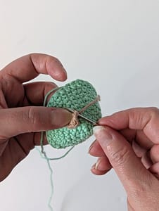 A small brown crochet circle being sewn onto a mint green crochet cone
