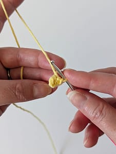 Two hands holding a crochet hook and some crochet stitches in yellow yarn