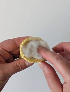 Toy stuffing being placed inside a crochet cone in yellow yarn